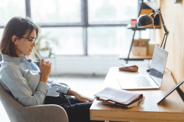 A woman deep in thought in front of her laptop looking at her notebook with her pen resting on her lips. Blog: What a "good enough" email setup actually looks like