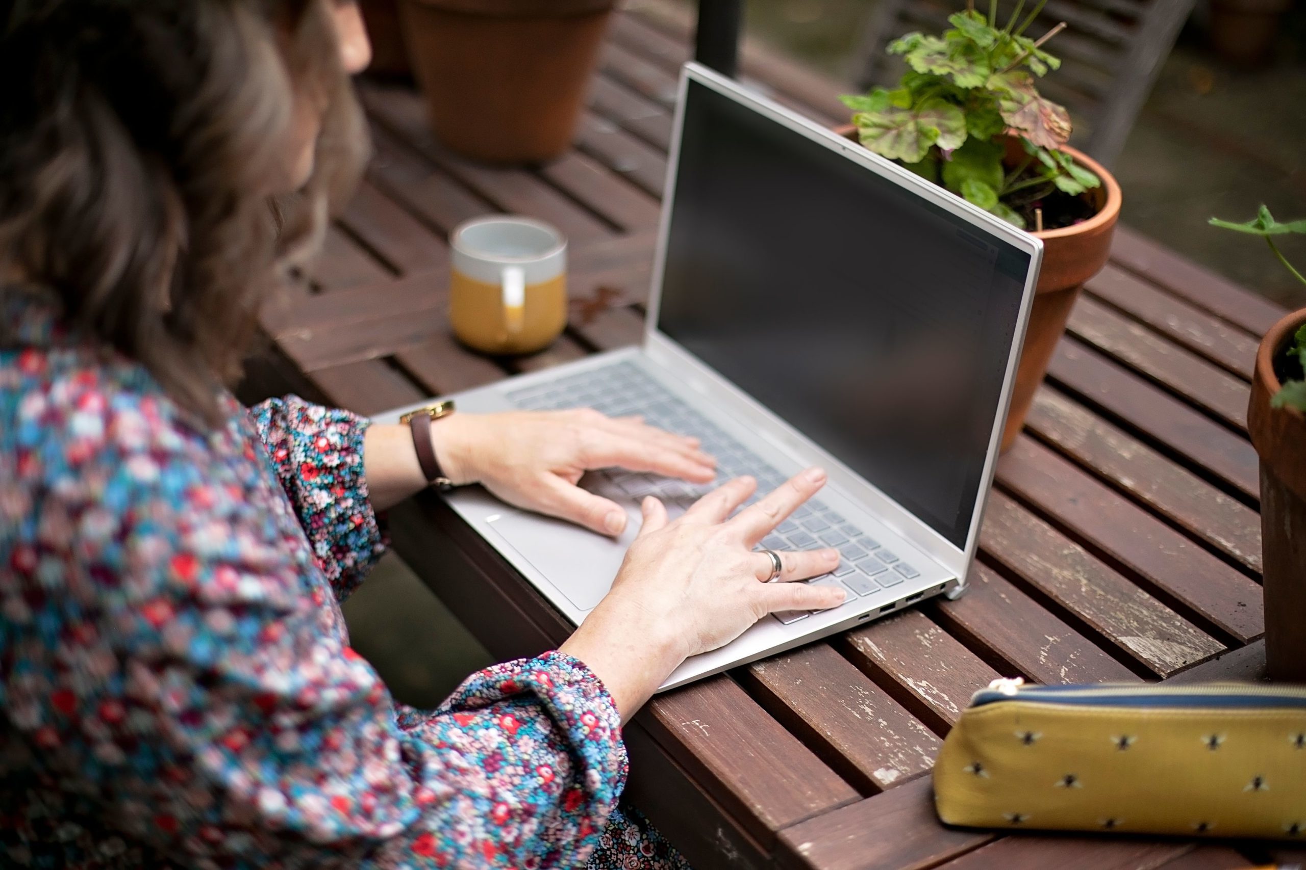 Image of Hannah Swierstra from the side working on a laptop, she is outside working on a garden table